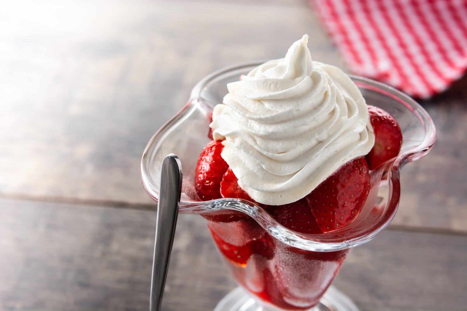 Strawberries and whipped cream in ice cream glass on wooden table